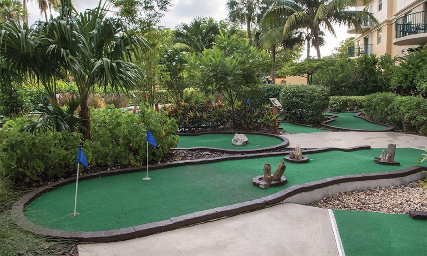 A miniature golf course with multiple holes, surrounded by lush greenery and palm trees.