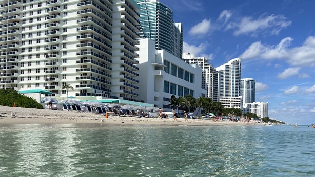 Un hotel sulla spiaggia con diversi piani, ombrelloni in riva al mare e vista libera sull'oceano.