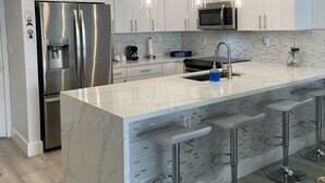 Una cucina moderna con mobili bianchi, un frigorifero in acciaio inox, un forno a microonde e una grande isola con sgabelli da bar.
