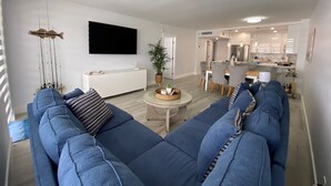 Un soggiorno moderno con un divano ampio, una televisione a schermo piatto e un'area pranzo con una cucina sullo sfondo.