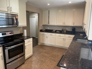 A kitchen with white cabinets, a black countertop, stainless steel appliances, and a tiled floor.