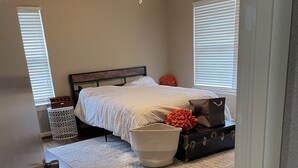 Un dormitorio con cama, ventilador de techo, ventana con persianas, mesita de noche y maleta.