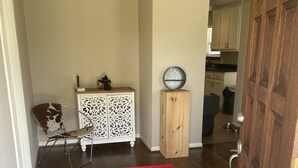 Un pasillo con suelo de madera, un armario blanco con diseños decorativos, un contenedor rojo y una puerta que da a una zona de cocina.