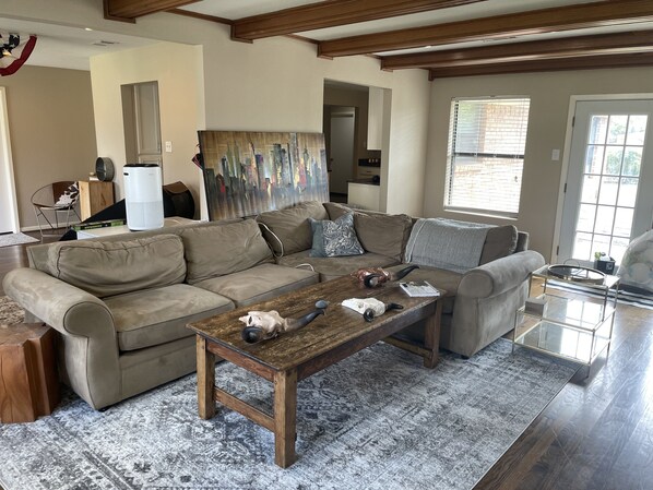 A spacious living room with a large sectional sofa, a wooden coffee table, and a cityscape painting on the wall.