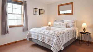 Quarto bem arrumado com cama, duas luminárias de apoio, janela com cortinas e dois quadros na parede.