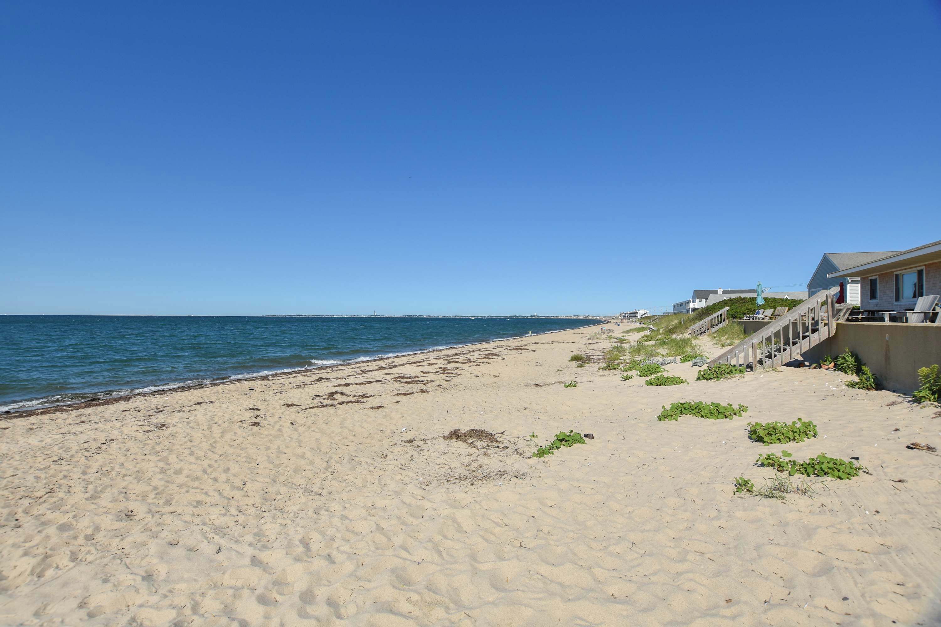 A beach with a building on the right side, featuring a staircase leading to a deck with lounge chairs.