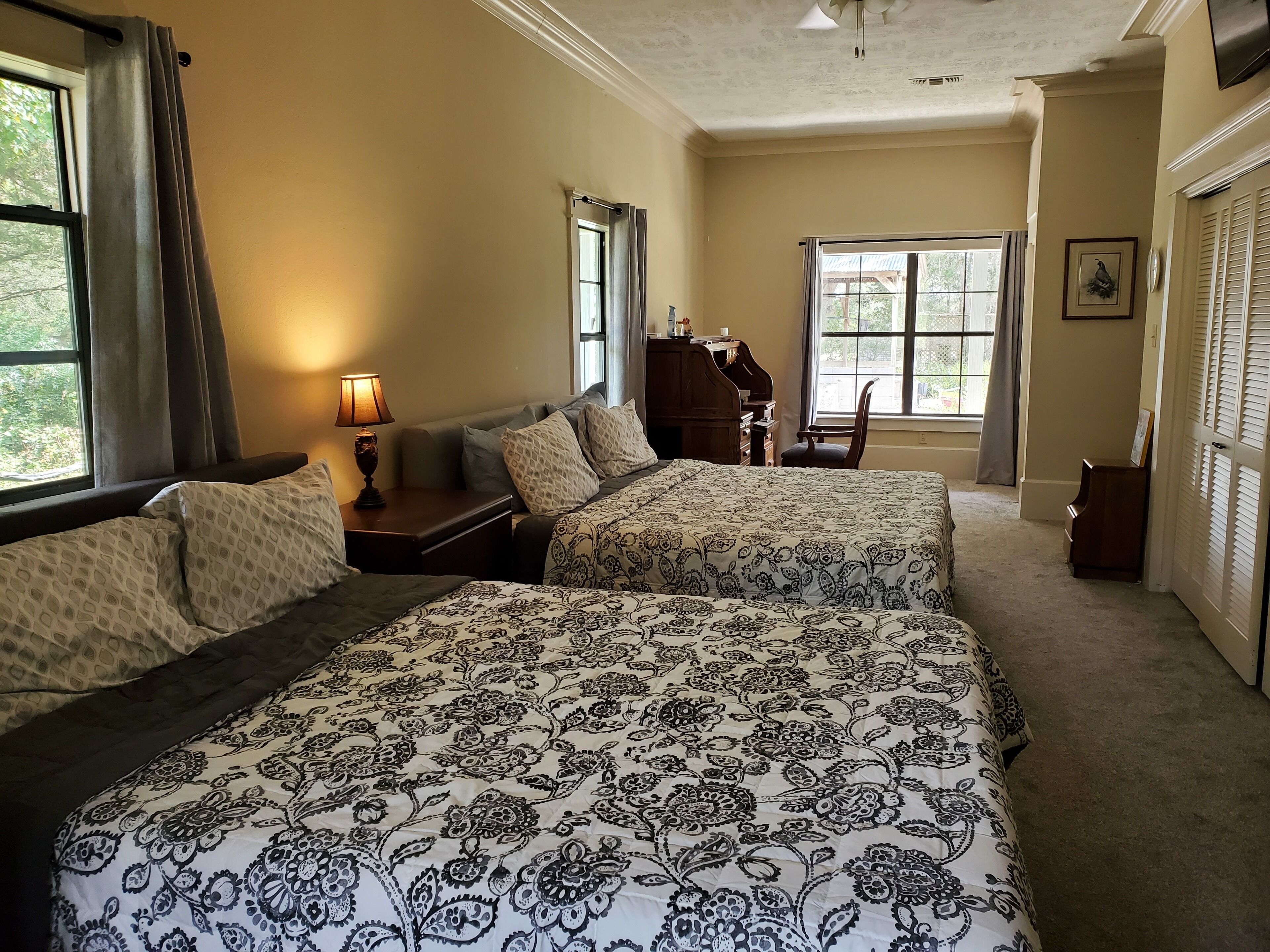 A hotel room with two beds, a desk, a chair, a dresser, and a window with a view of greenery.