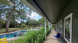 A covered outdoor area with a pool, chairs, and a pathway leading to a building. - Quaint 4 Bedroom Farmhouse near Round Top, New Ulm (Cat Spring)