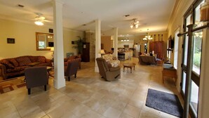 A spacious living area with a sofa, chairs, a coffee table, and a dining table. There is a kitchen in the background with a refrigerator and cabinets. - Quaint 4 Bedroom Farmhouse near Round Top, New Ulm (Cat Spring)
