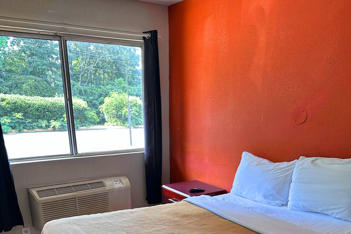 A hotel room with a bed, a window with curtains, a heater, and a red wall.