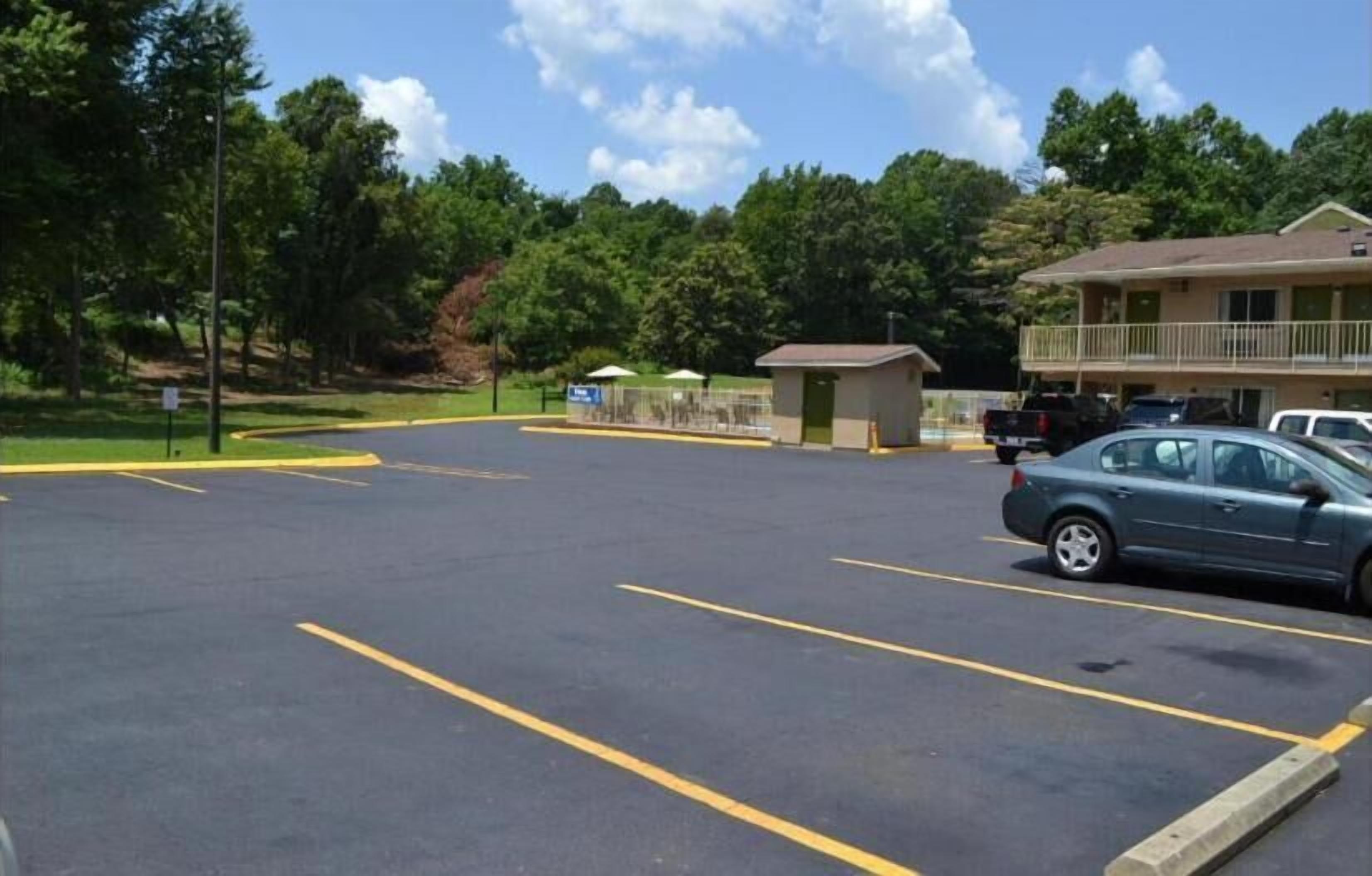 A parking lot with marked spaces, a small building, and a larger building with a balcony in the background.