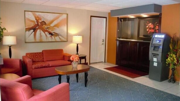 A hotel lobby with a red sofa, a coffee table, a painting, a reception desk, and a self-service kiosk. - High Point Arcadia Inn (High Point)