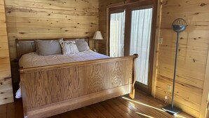 Ein Bett mit hölzernem Gestell, einem Kopfteil, einer Nachttischlampe und einer Stehlampe in einem Raum mit Holzwänden und -böden.
