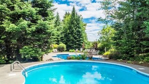 Ein Swimmingpool, umgeben von Bäumen und einer Terrasse mit Liegestühlen.
