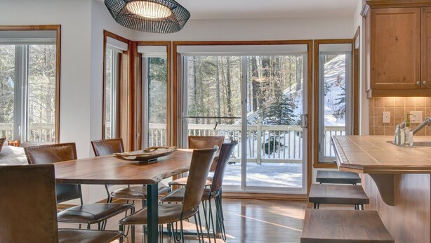 Ein geräumiger Essbereich mit Holztisch und -stühlen, großen Fenstern mit Blick auf eine verschneite Terrasse und einer Küche mit Holzschränken.