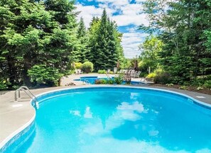 Una piscina rodeada de árboles y un patio con sillas de descanso.