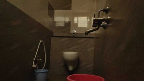 Une salle de bain avec des toilettes, un bidet et un seau rouge.
