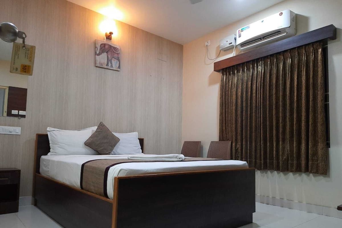Una habitación de hotel con una cama, aire acondicionado de pared, lámpara de pared y un cuadro de un elefante.