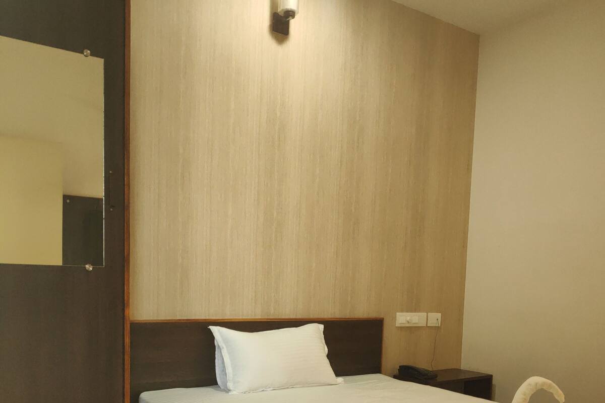 Habitación de hotel con una cama de madera, una mesita de noche, una lámpara de pared y un espejo.