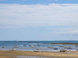 A beach with several boats anchored in shallow water, a sandy shore, and a distant shoreline with a breakwater. - Les palmiers by Interhome (Saint Philibert)