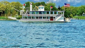 A riverboat with a covered deck and multiple levels, docked at a pier.