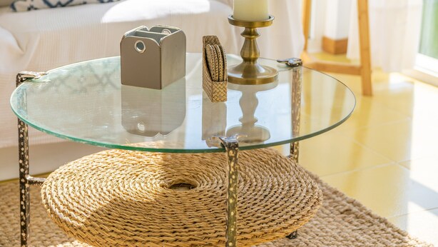 A glass-top coffee table with a woven placemat, a candle holder, and a smartphone on it.