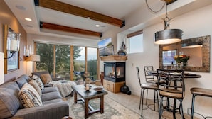 Amplia sala de estar con chimenea, comedor con taburetes de bar y un ventanal con vistas al exterior.