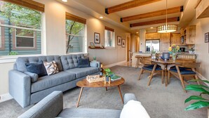 Een moderne woonkamer met een grijze bank, een houten salontafel en een eethoek met een houten tafel en stoelen.