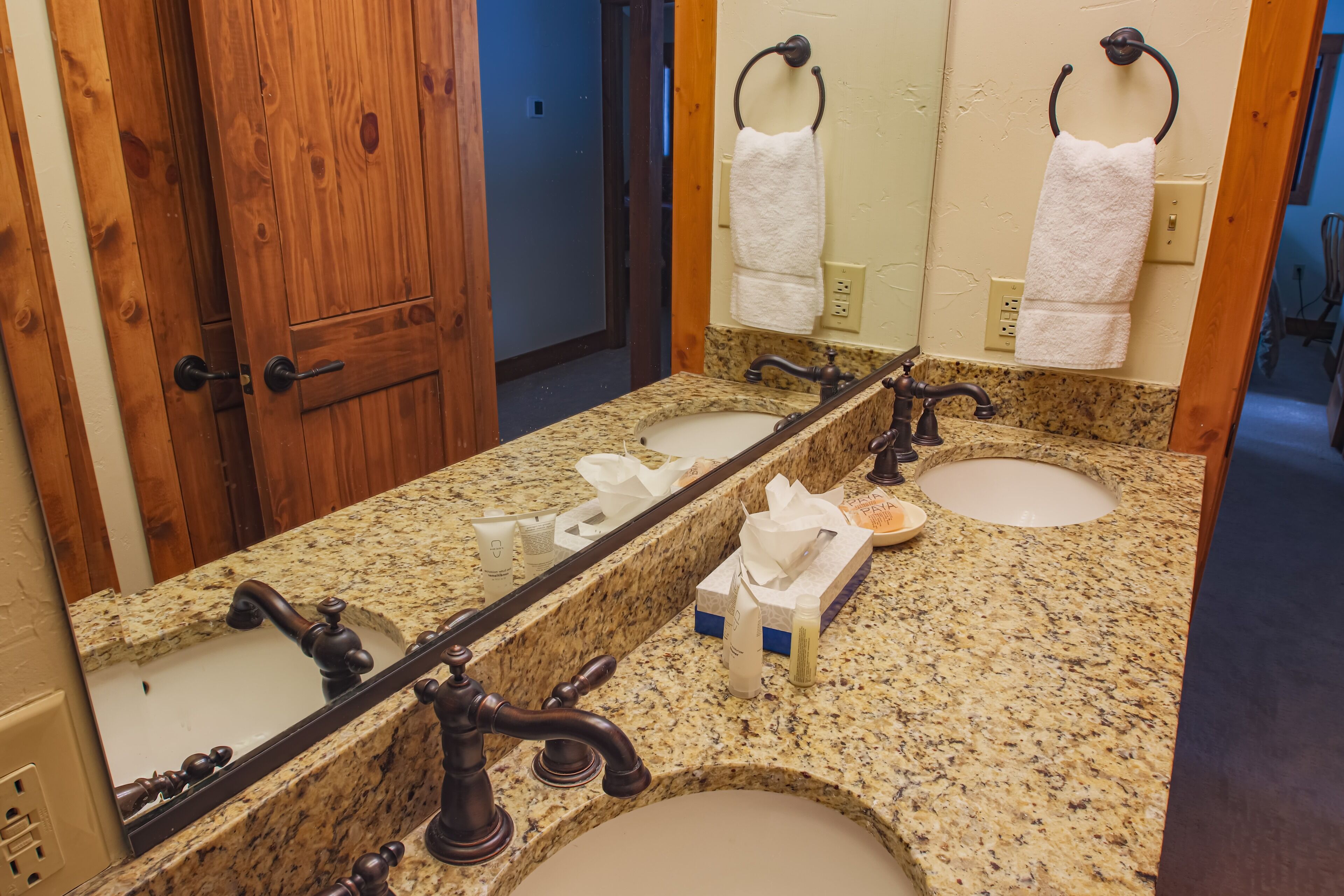 A bathroom with two sinks, a large mirror, wooden door, and a towel rack.
