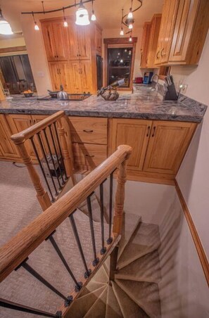 A kitchen with wooden cabinets, a granite countertop, and a wooden staircase.