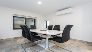 A conference room with a white table, black chairs, a window, and an air conditioning unit. - Across The Road From The Beach (Inverloch)