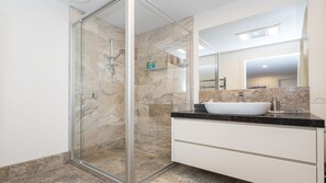 A modern bathroom with a glass-enclosed shower, a white vanity with a large mirror, and marble flooring.