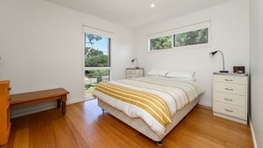Une chambre avec un plancher en bois, un lit avec une literie à rayures, une table de chevet, un bureau et une commode.