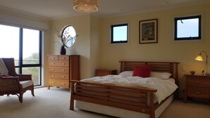 A bedroom with a wooden bed, a dresser, a chair, and a window with a view. - Stunning Sea Views on Surf (CAPE PATERSON)