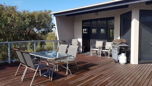 A deck with a glass table and chairs, a barbecue grill, and a white water dispenser. - Stunning Sea Views on Surf (CAPE PATERSON)