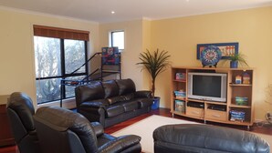 A living room with a leather sofa, a television, and a piano. - Stunning Sea Views on Surf (CAPE PATERSON)