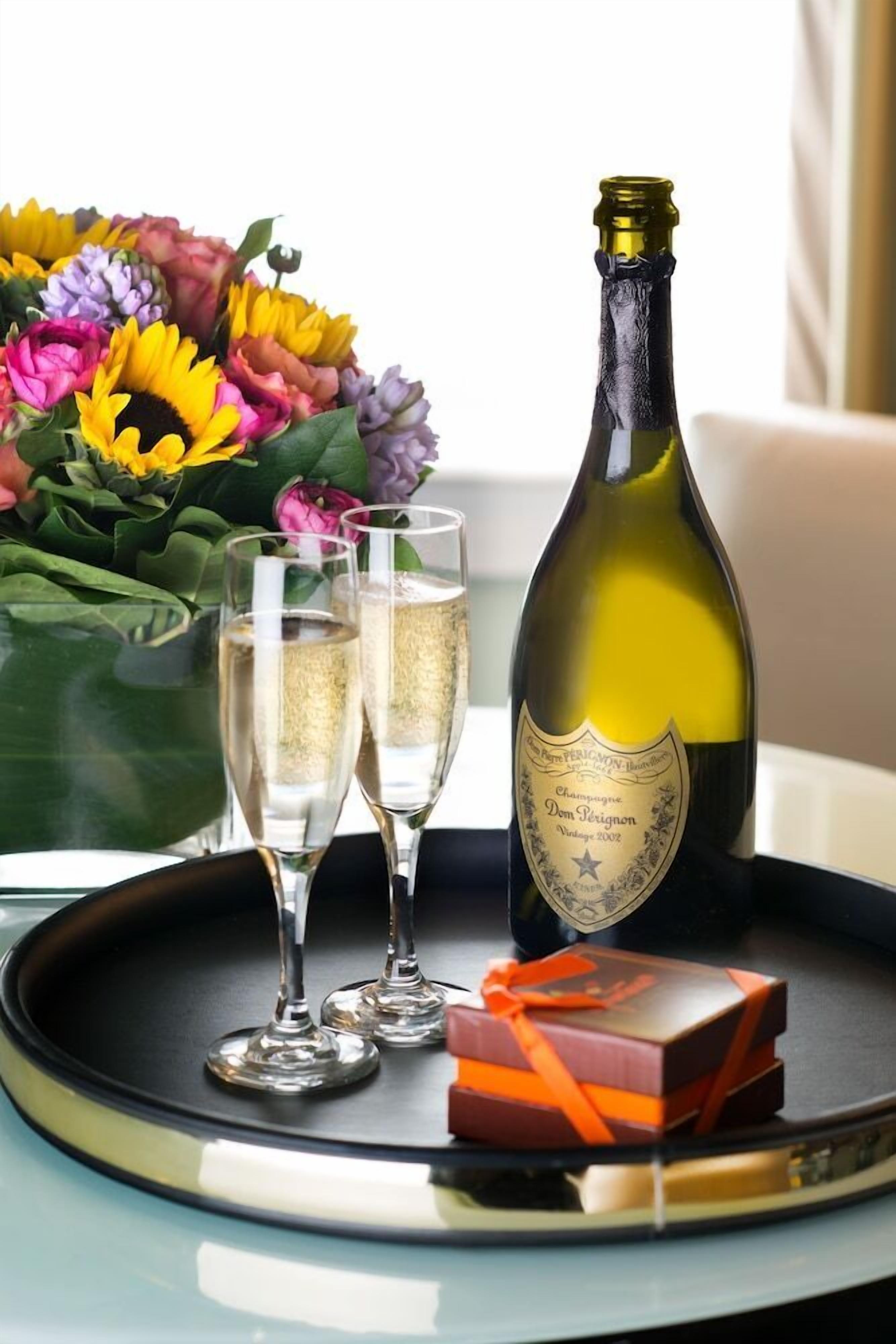 A bottle of Dom Pérignon champagne, two glasses of champagne, a bouquet of flowers, and a small gift box on a tray.