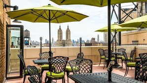 Une terrasse extérieure avec des tables et des chaises, des parasols jaunes et une vue sur les toits de la ville.