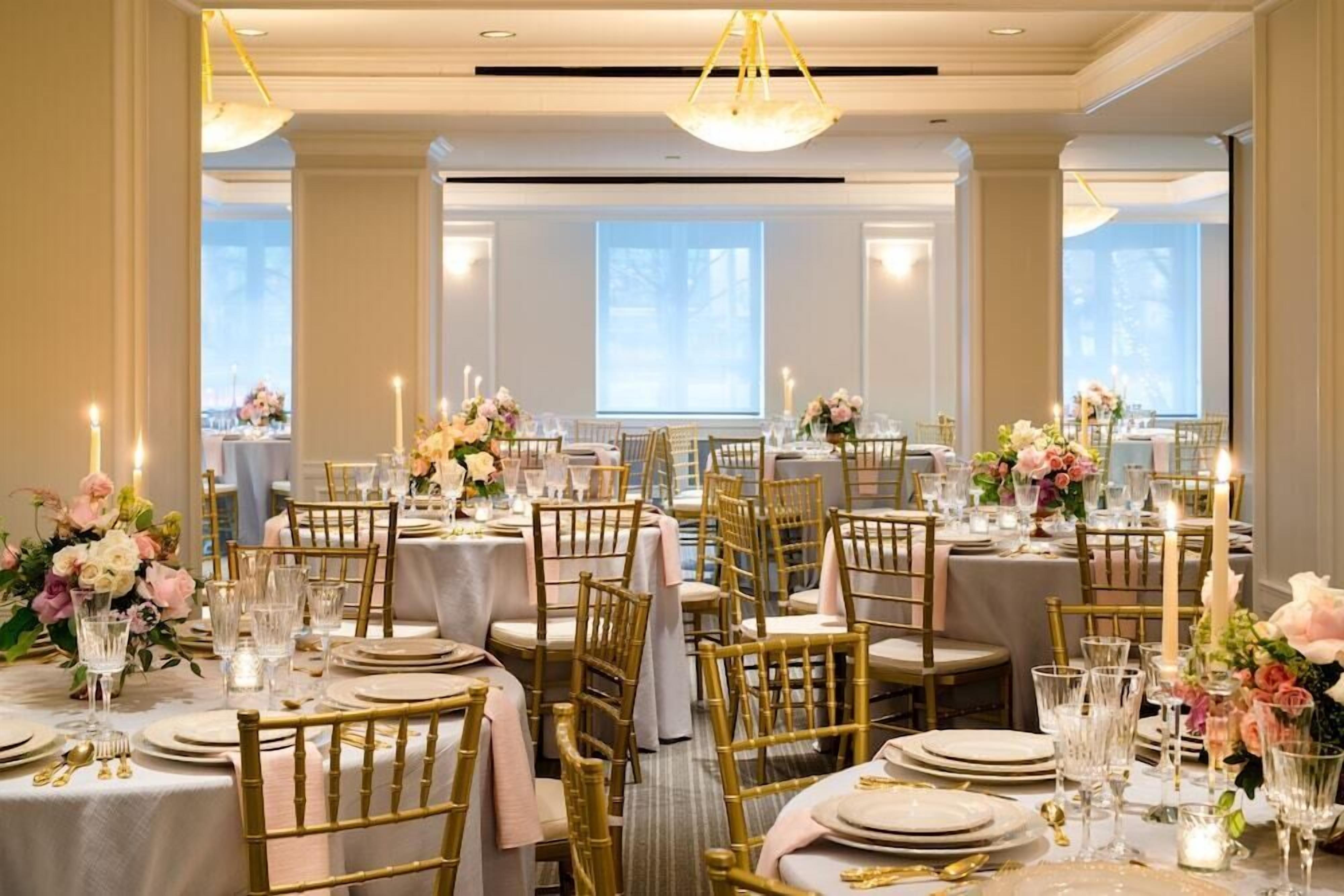 A banquet hall with round tables, gold chairs, and floral centerpieces.