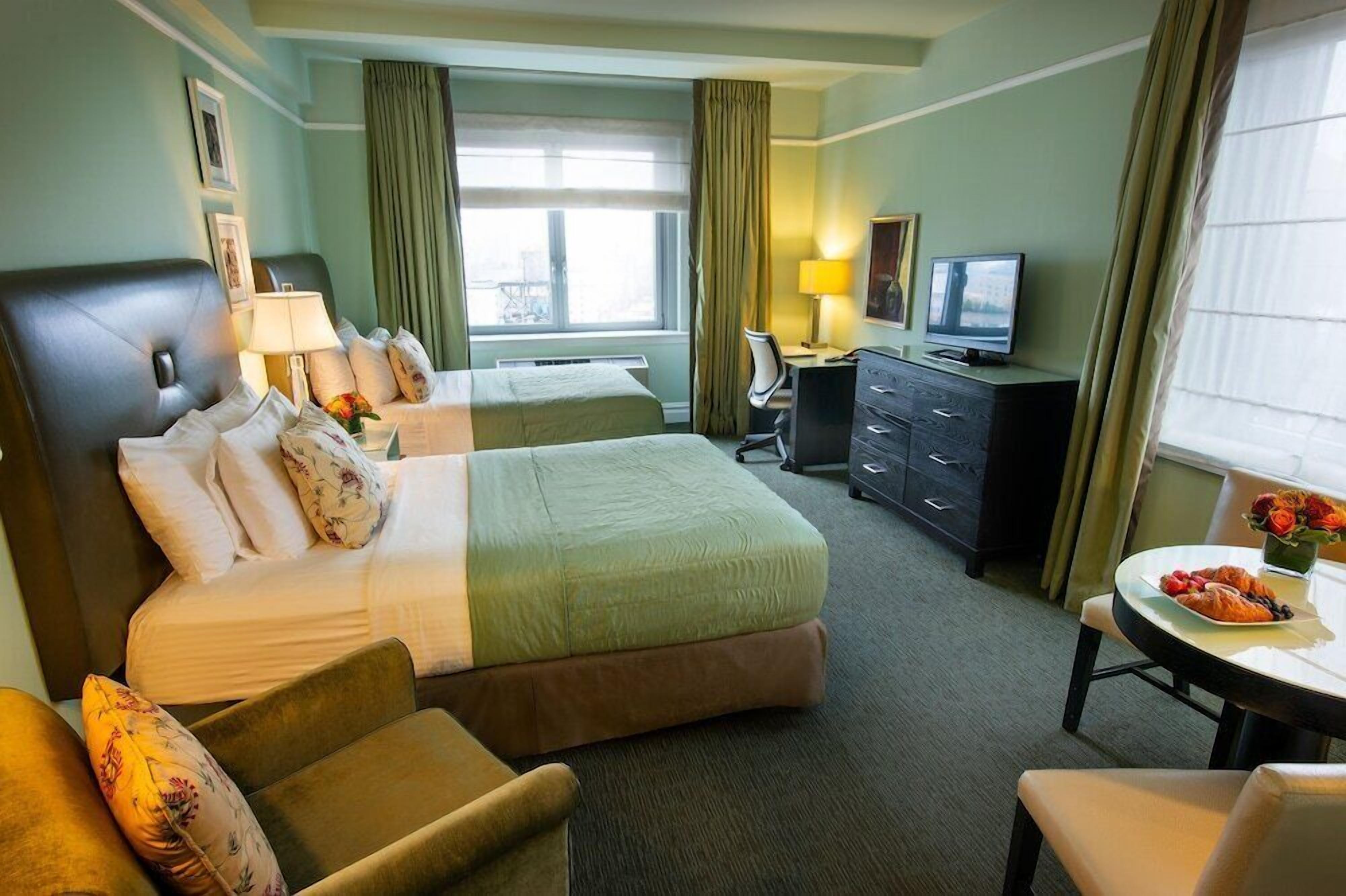 Ein Hotelzimmer mit zwei Betten, einem Schreibtisch, einem Fernseher und einem Esstisch mit einem Teller Essen.