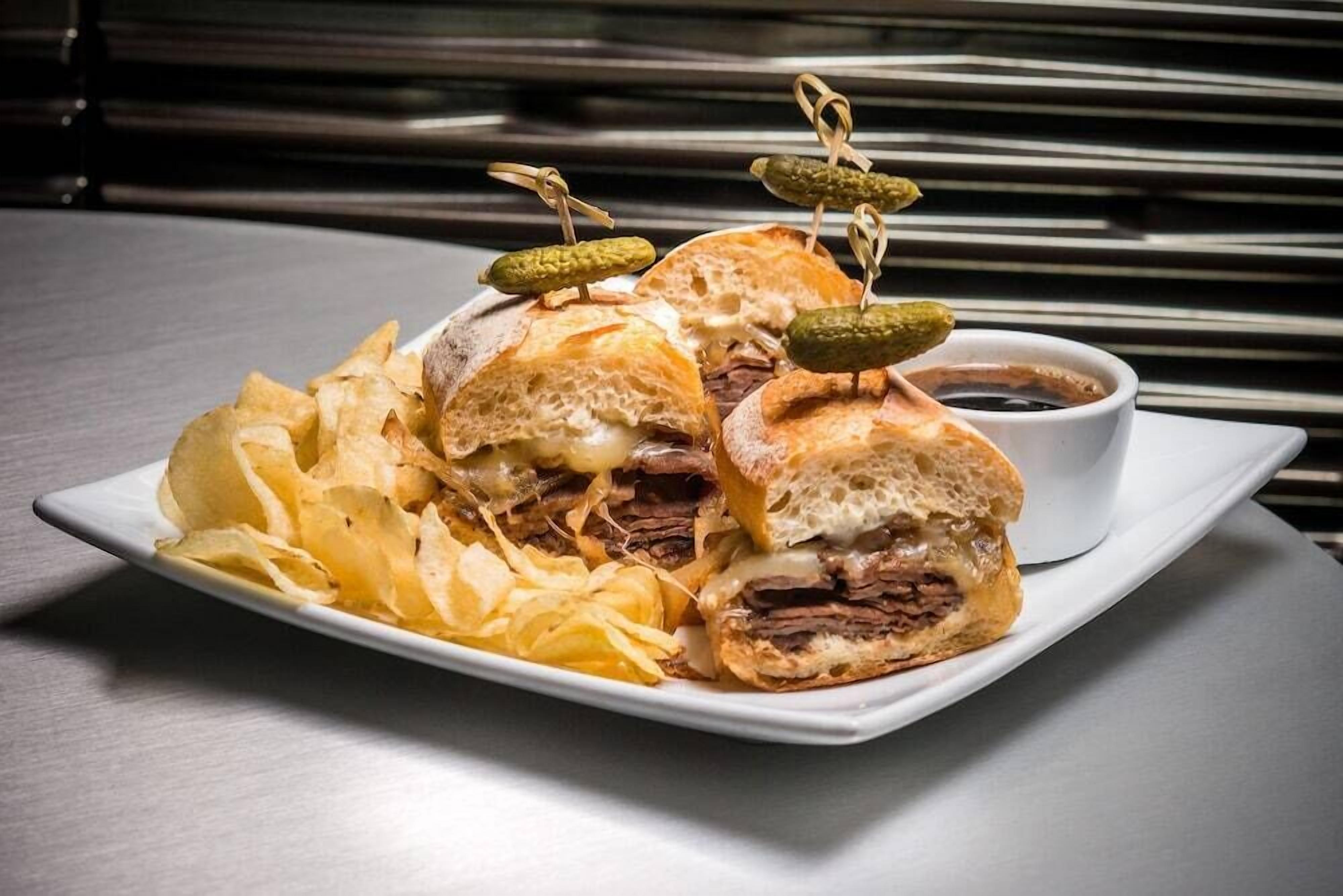A plate with a sandwich, chips, and a small bowl of sauce.