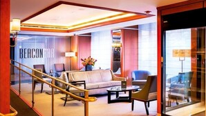 Un hall d’hôtel avec un escalier, un espace salon et un mur de verre sur lequel on peut lire le texte « BEACON BAR ».