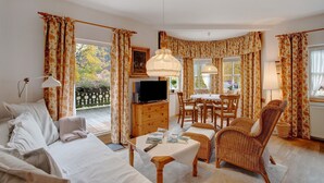 A cozy room with a bed, a dining table, a wicker chair, and a TV. - Vacation apartment "Seeberg - House Annamirl" with beautiful south terrace (Bayrischzell)