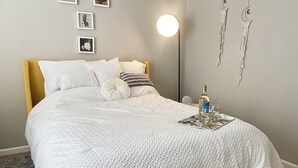 Ein ordentlich bezogenes Bett mit weißer Decke, einer Nachttischlampe und einem Tablett mit Gläsern und einer Flasche.