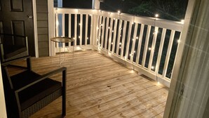 Eine Holzterrasse mit Geländer, einem kleinen Tisch und einem Stuhl.