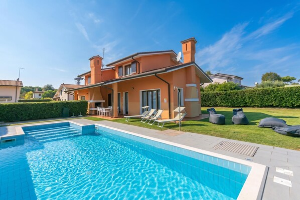 Une propriété résidentielle dotée d’une piscine, de chaises longues et d’une pelouse bien entretenue.