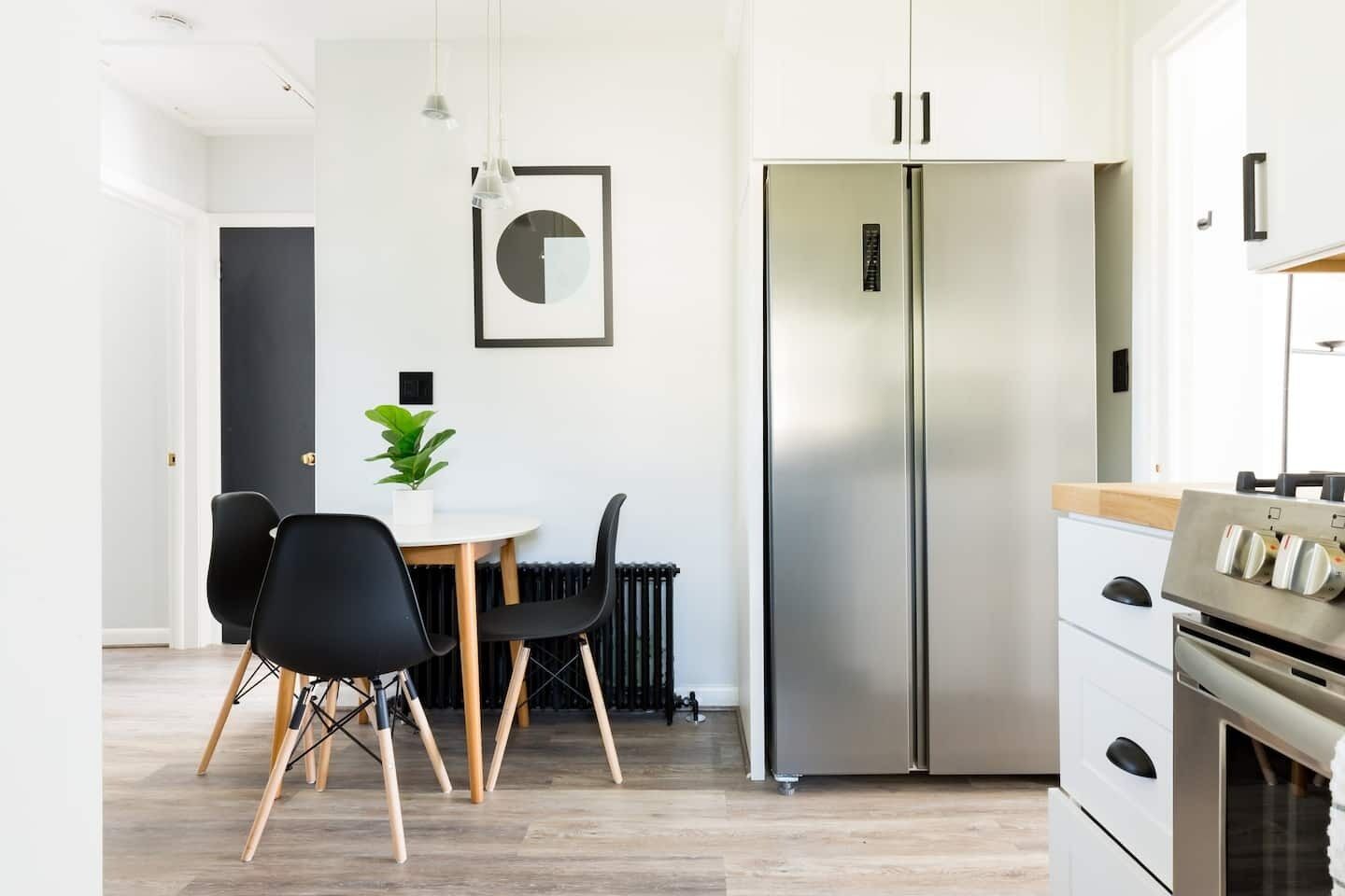 A modern kitchen with a stainless steel refrigerator, a dining table with chairs, and a potted plant.