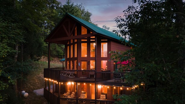 A cabin with a balcony, string lights, and a view of the surrounding forest. - Cozy cabin w/ Hot tub, Arcade, Wi-Fi, Air Hockey & Views (Sevierville)