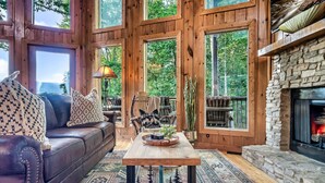 A cozy cabin interior with a leather sofa, a wooden table, and a stone fireplace. - Cozy cabin w/ Hot tub, Arcade, Wi-Fi, Air Hockey & Views (Sevierville)