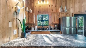 A kitchen with wooden walls, a marble countertop, and a stainless steel refrigerator. - Cozy cabin w/ Hot tub, Arcade, Wi-Fi, Air Hockey & Views (Sevierville)